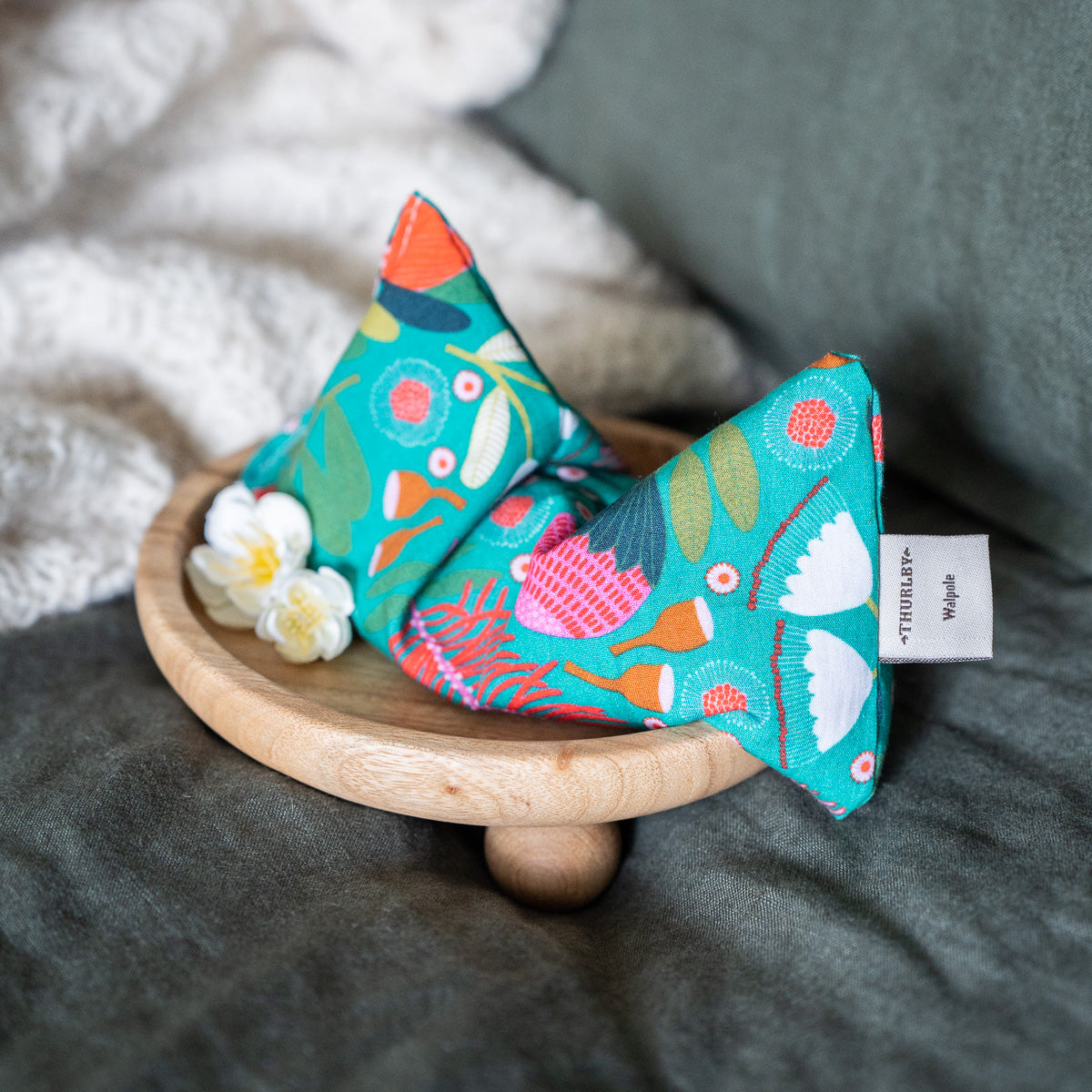 Patterned eye pillow on wooden stand with blossoms. Linen bedding in the background 