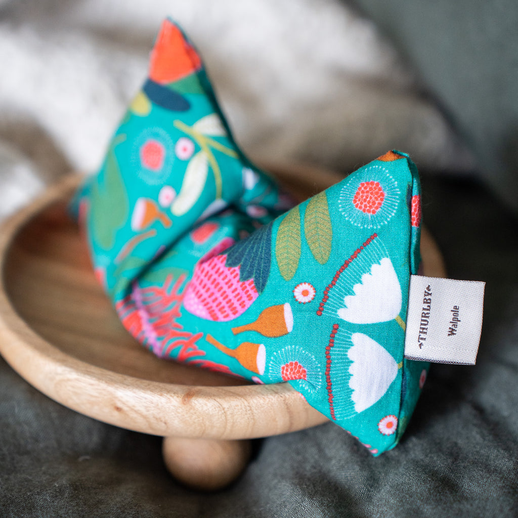 Patterned blue eye pillow, close up of design. Eye pillow resting on a wooden stand. 