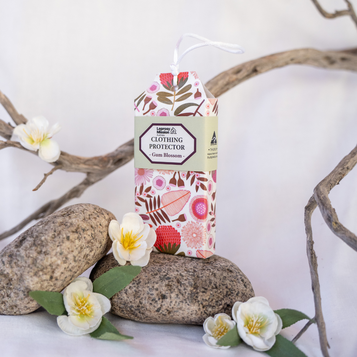 Packaging of clothing protector with floral design on a white background with stones and flowers.