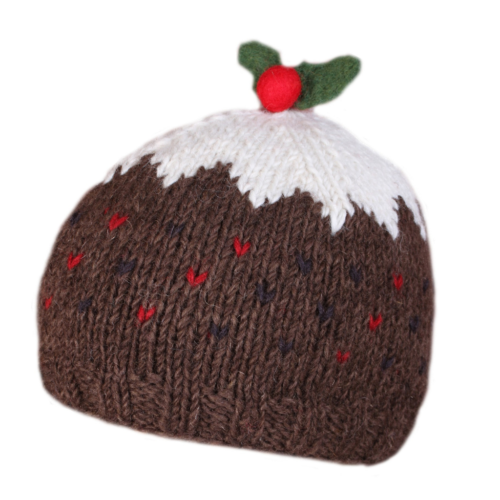 A knitted pudding hat shaped like a Christmas pudding, with a brown body, white frosting, red berries, and green holly leaves on top, shown on a plain white background.