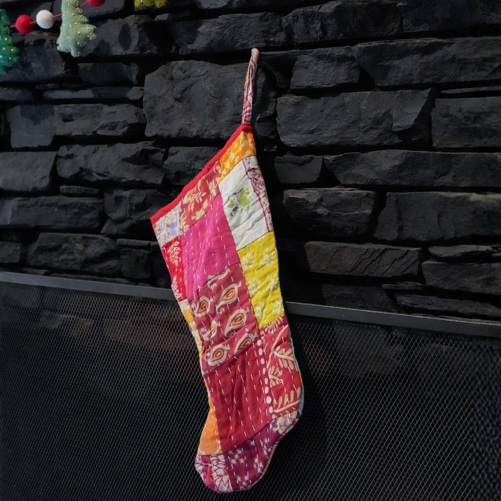 A colorful patchwork quilted Christmas stocking hanging from a hook on a dark stone fireplace wall.