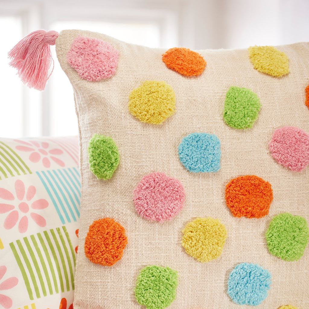 Decorative pillow with colorful pom-poms on a floral-patterned couch.