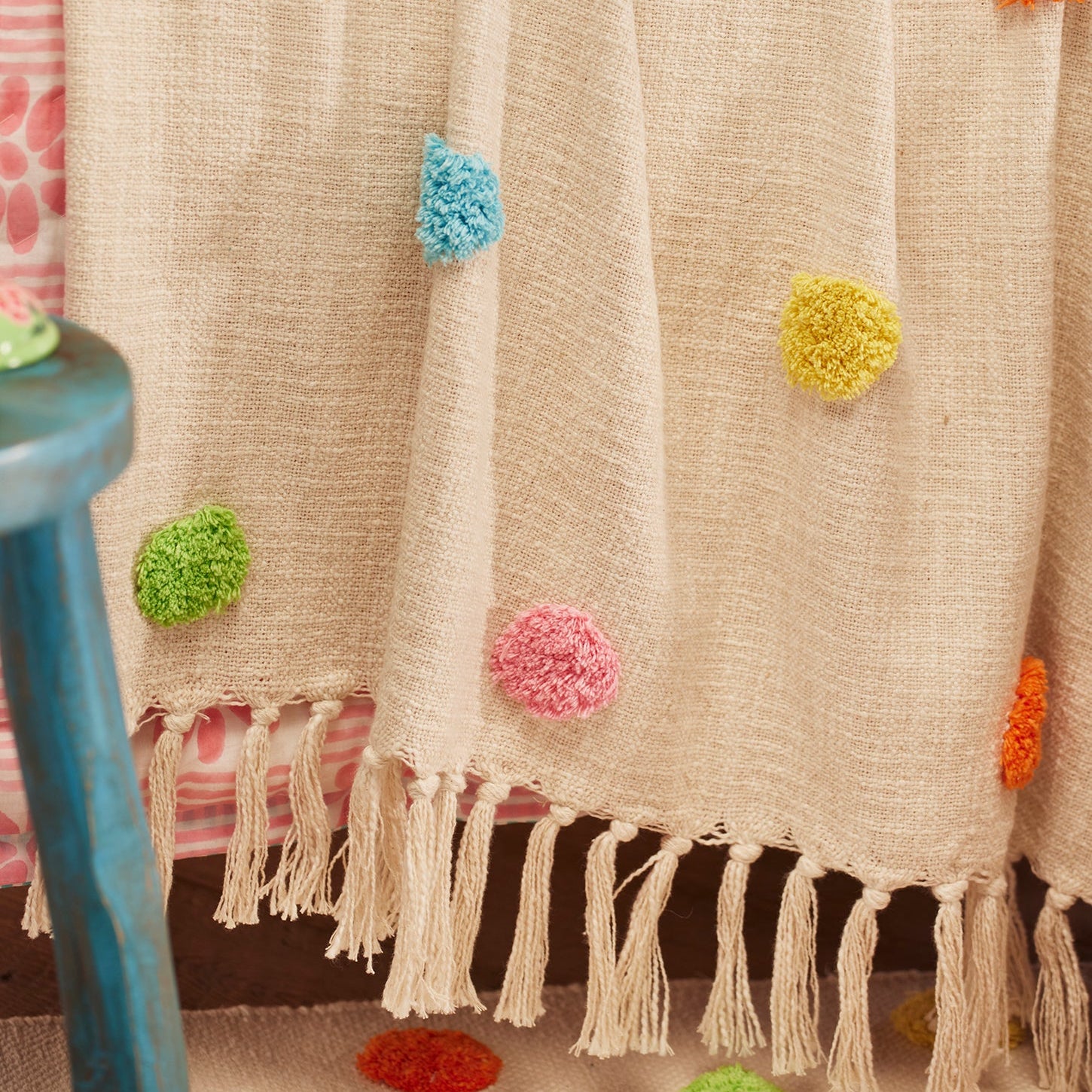 Beige blanket with colorful pom-poms on a chair
