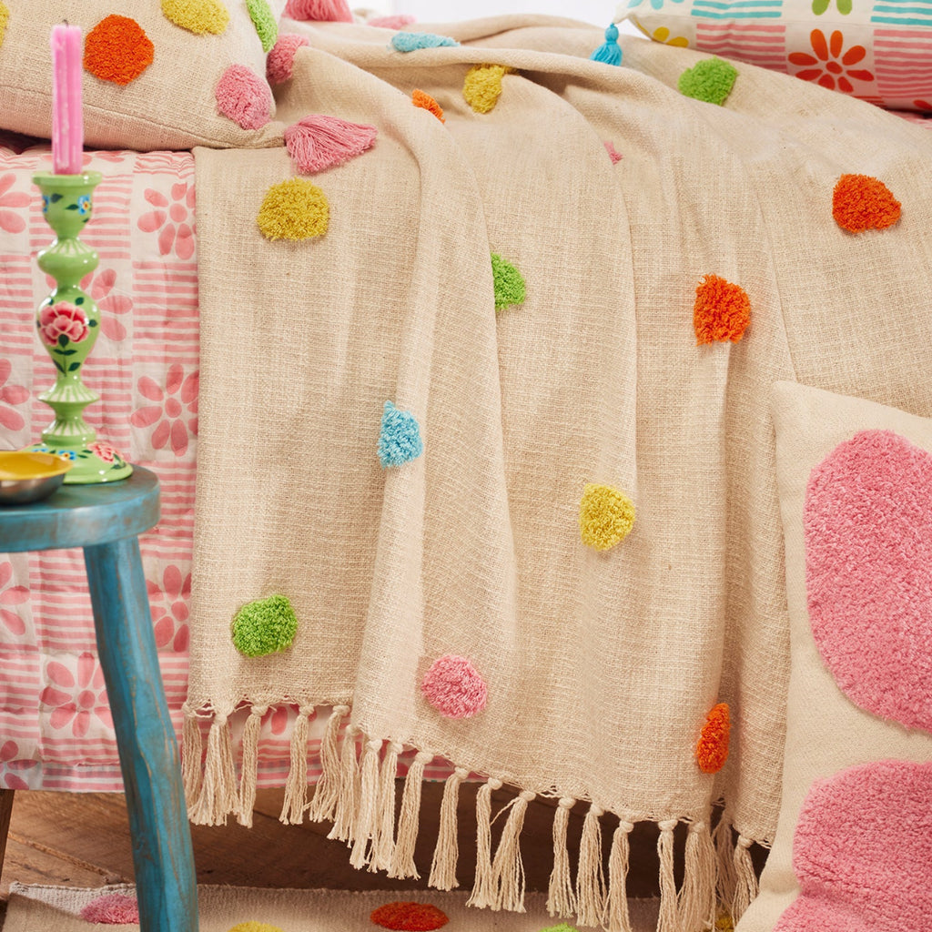 Decorative bedspread with colorful pom-poms on a bed in a bright room.