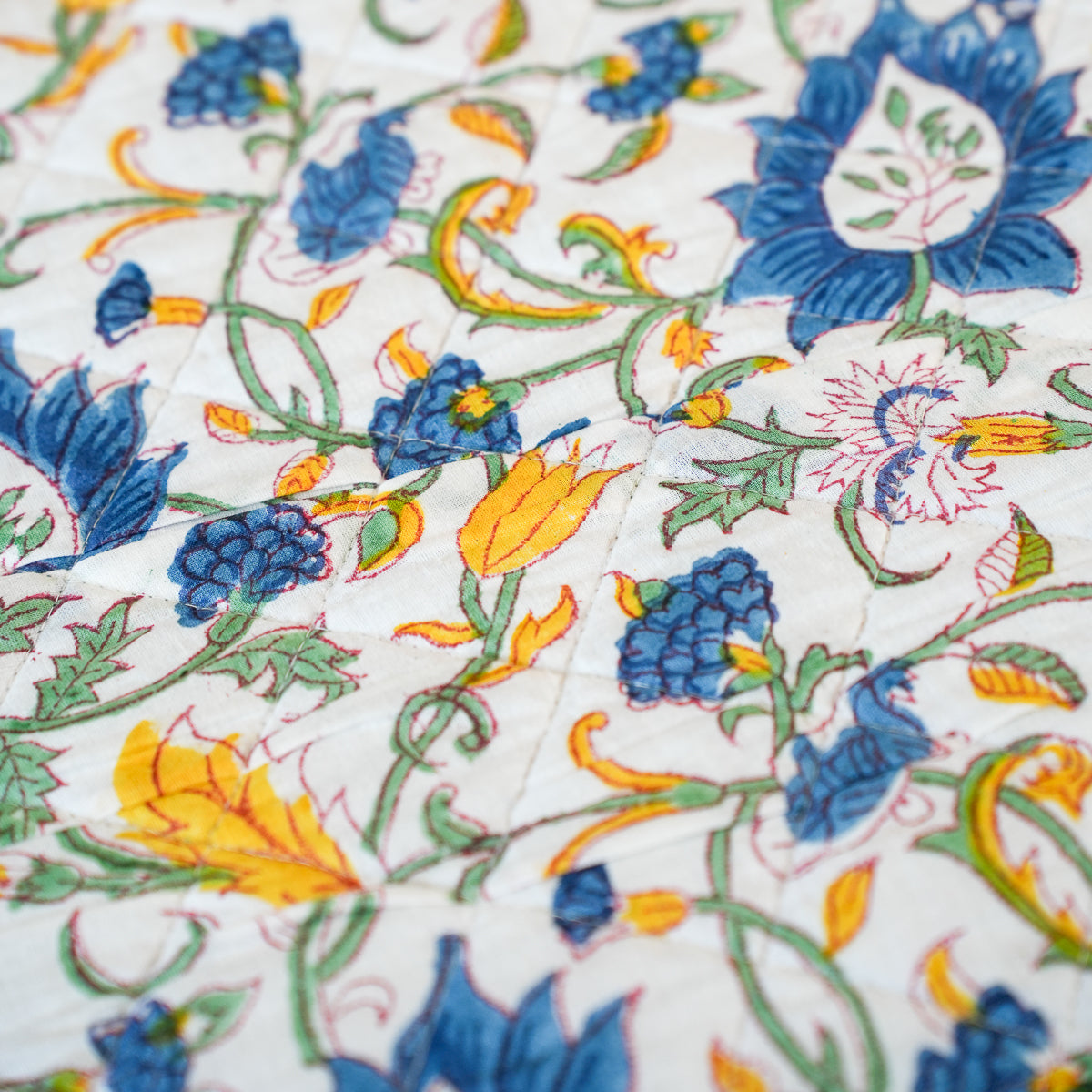 A close-up of a white quilted fabric featuring a colorful floral and vine pattern with blue, yellow, and green embroidered details.