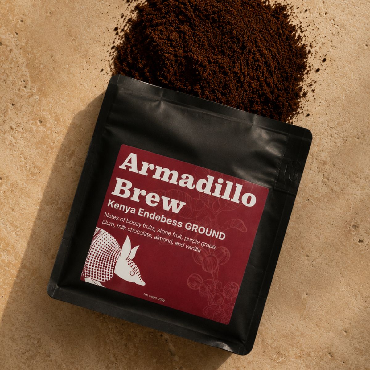 Open black coffee bag labeled 'Armadillo Brew Kenya Endeless' on a beige surface with ground coffee.