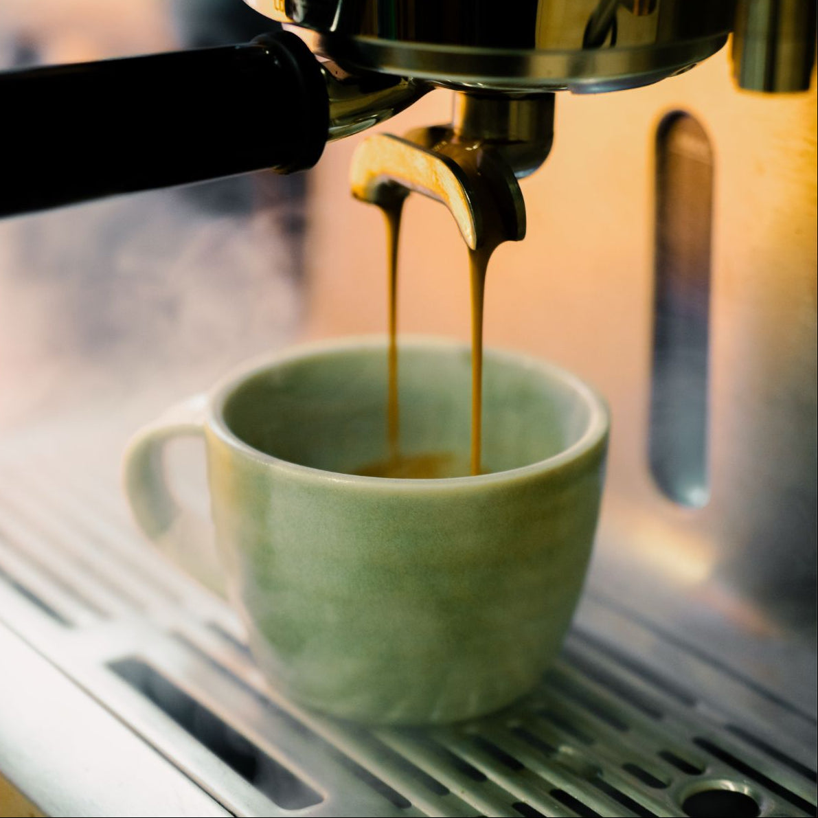 Espresso being poured into a green mug from an espresso machine.