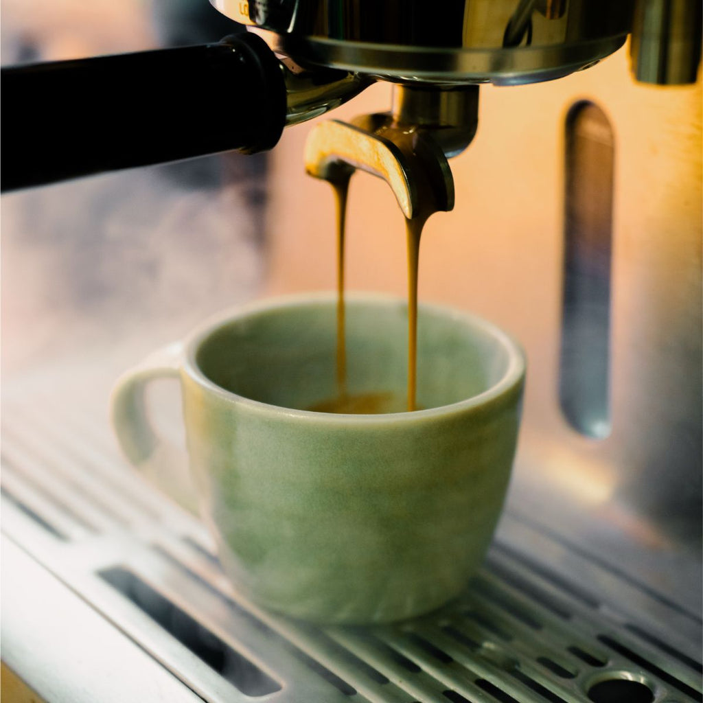 Espresso being poured into a green mug from an espresso machine.