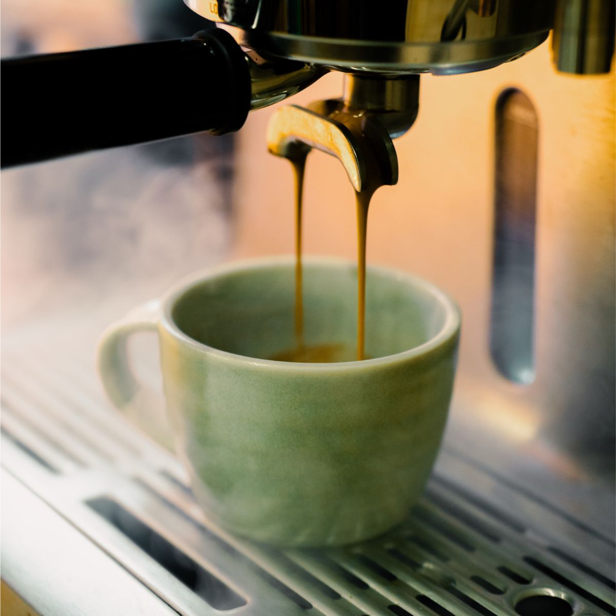 Espresso being poured into a green mug from an espresso machine.
