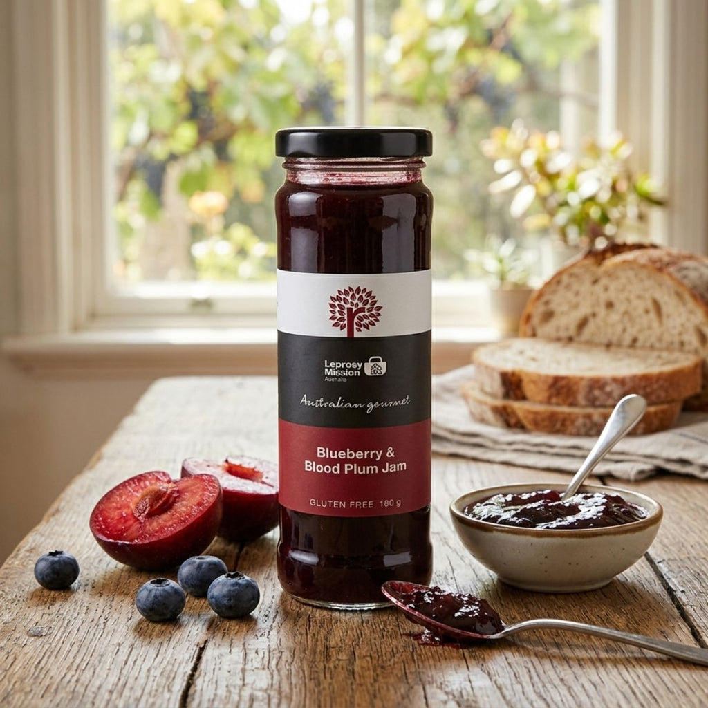 Jar of blueberry and blood plum jam on a wooden table with fruits and bread in the background.