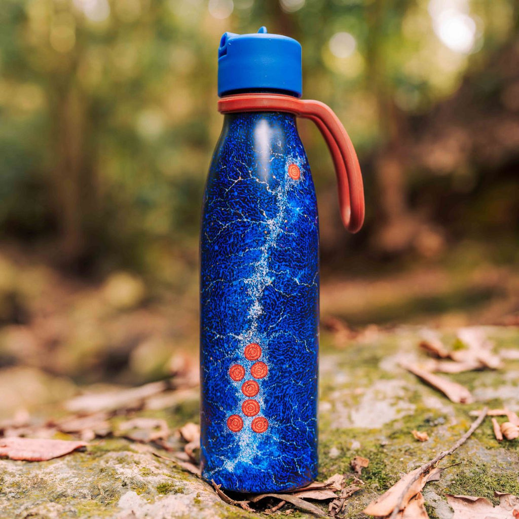 Blue water bottle with red patterns on a rock in a forest setting