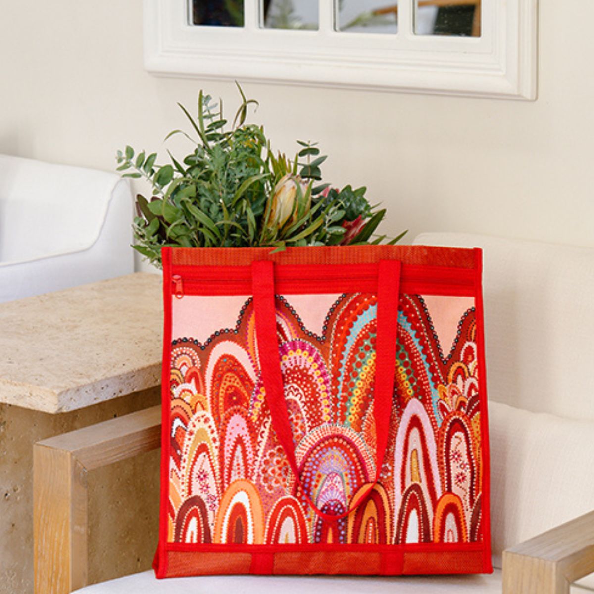 Decorative red bag with colorful patterns holding a plant on a table.