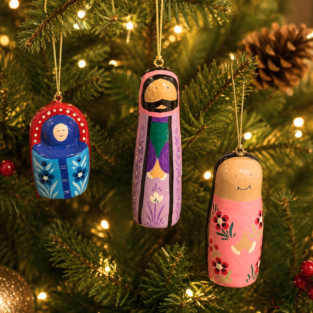 Three hand-painted wooden nesting doll Christmas ornaments hanging on a lit green Christmas tree.