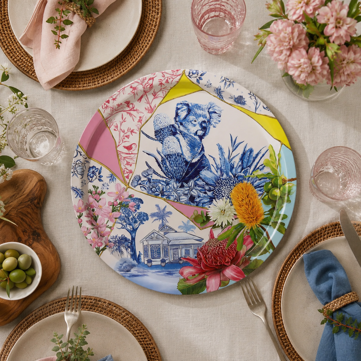 Colorful decorative plate with a koala design on a table setting with flowers and cutlery.