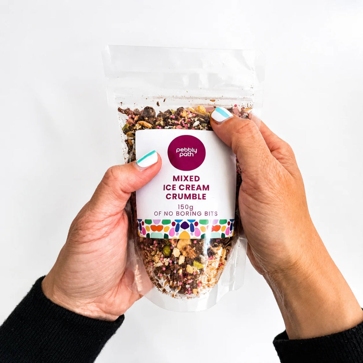 A person holding a clear stand-up pouch of Perky Port Mixed Ice Cream Crumble. The hands, which have light blue nail polish, hold the package against a clean white background.