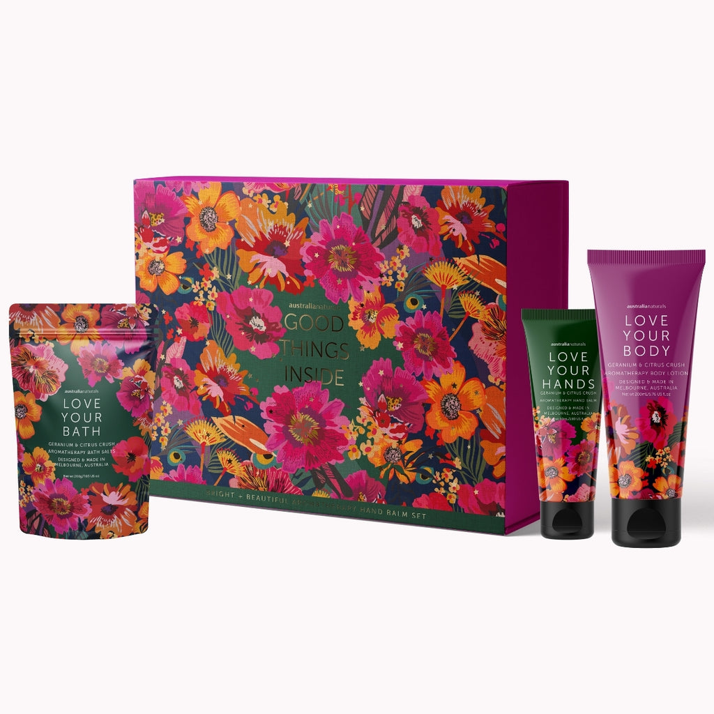 A Bath + Beauty Good Things Inside gift set featuring a large floral-patterned box, a bath soak pouch, and two hand/body care tubes labeled Love Your Body, Love Your Hands, and Love Your Bath on a light gray background.
