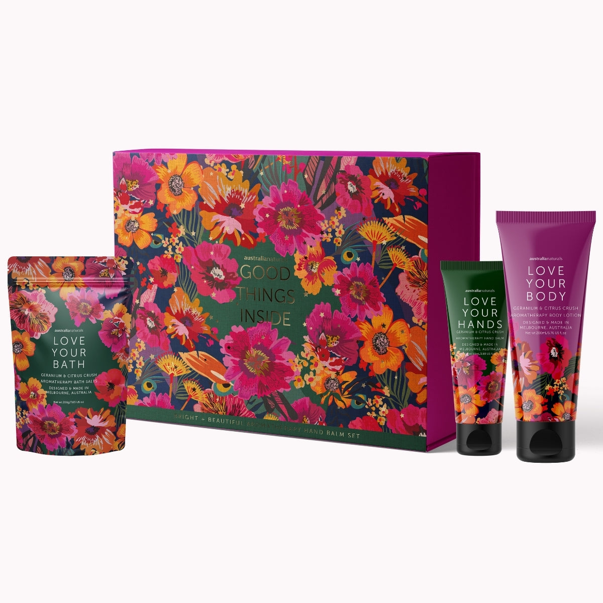 A Bath + Beauty Good Things Inside gift set featuring a large floral-patterned box, a bath soak pouch, and two hand/body care tubes labeled Love Your Body, Love Your Hands, and Love Your Bath on a light gray background.