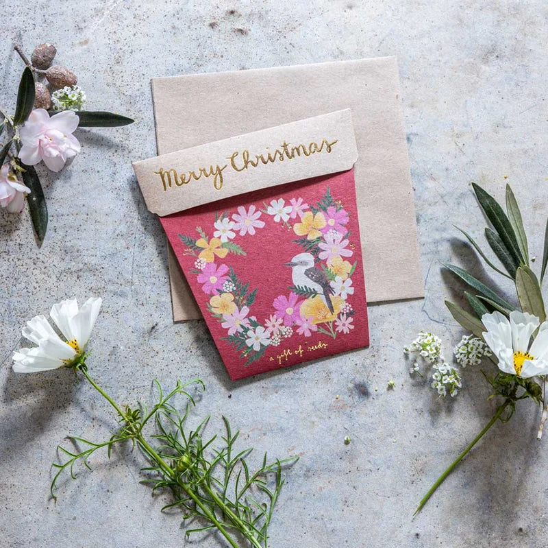 Greeting card with floral design and 'Merry Christmas' envelope on a textured surface with flowers.