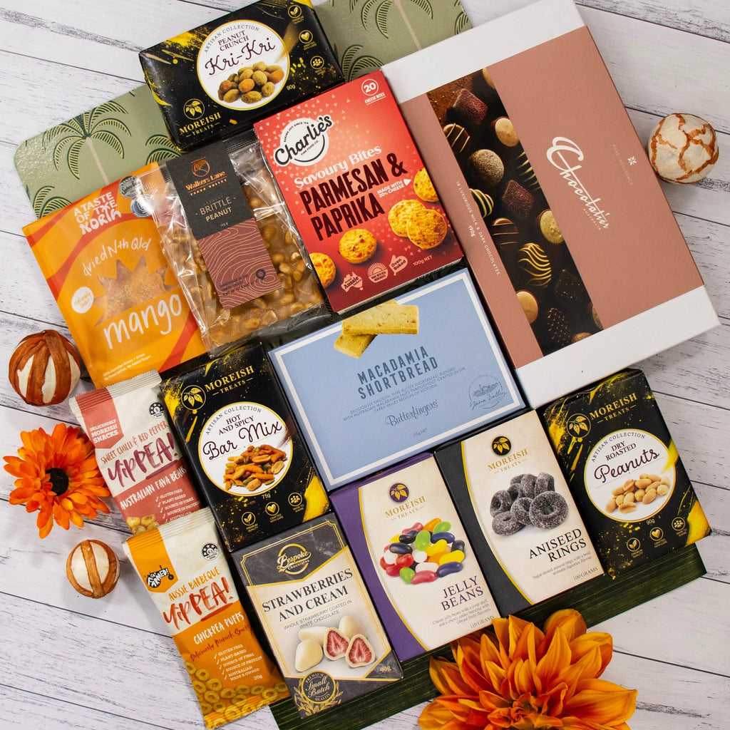 An assortment of gourmet snacks and chocolates arranged in a flat lay on a white wood background, featuring brands like Morfini, Charlies, and Krueken's.