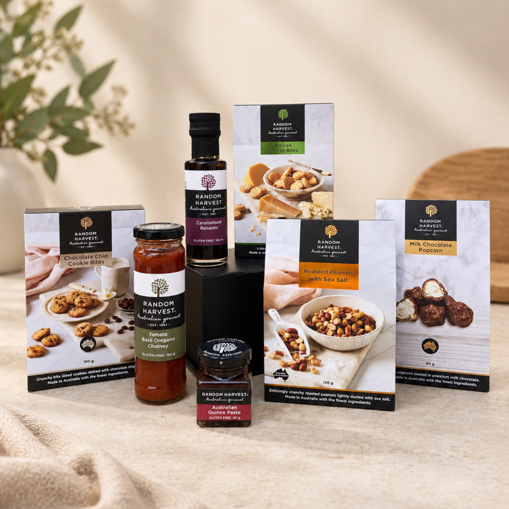 A curated assortment of Rangoon Harvest gourmet food products, including jars of chutney and preserves, a bottle of dressing, and multiple boxes of assorted nuts, chocolates, and spreads, arranged on a neutral beige fabric surface with soft, warm lighting.
