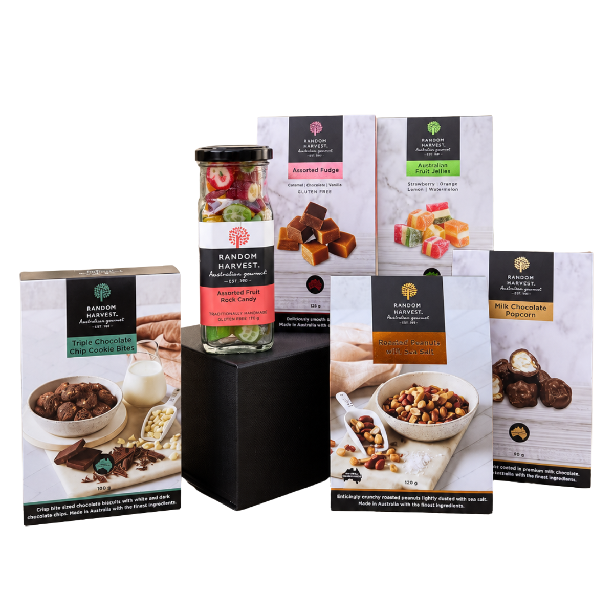 A gift set of Random Harvest chocolate products arranged on a white background, including a jar of assorted fruit nibs on a black pedestal box, several chocolate-coated biscuit boxes, and candy pouches.
