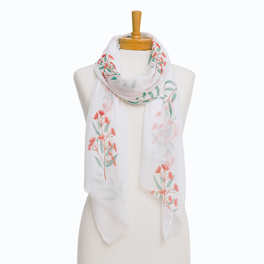 A white scarf with a delicate pink and green floral pattern, draped on a cream-colored mannequin torso with a wooden neck cap against a plain white background.
