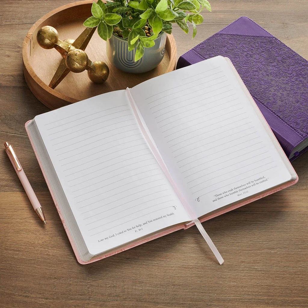 Open notebook on a wooden surface with a pen and decorative items.