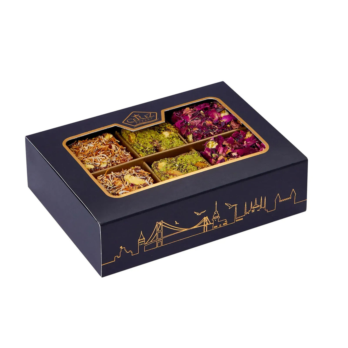 A black gift box of assorted tea or spice blends with a clear window showing six compartments filled with different dried blends, including rose petals, green herbs, and golden-brown spices. The box has gold detailing, including a city skyline illustration on the side.