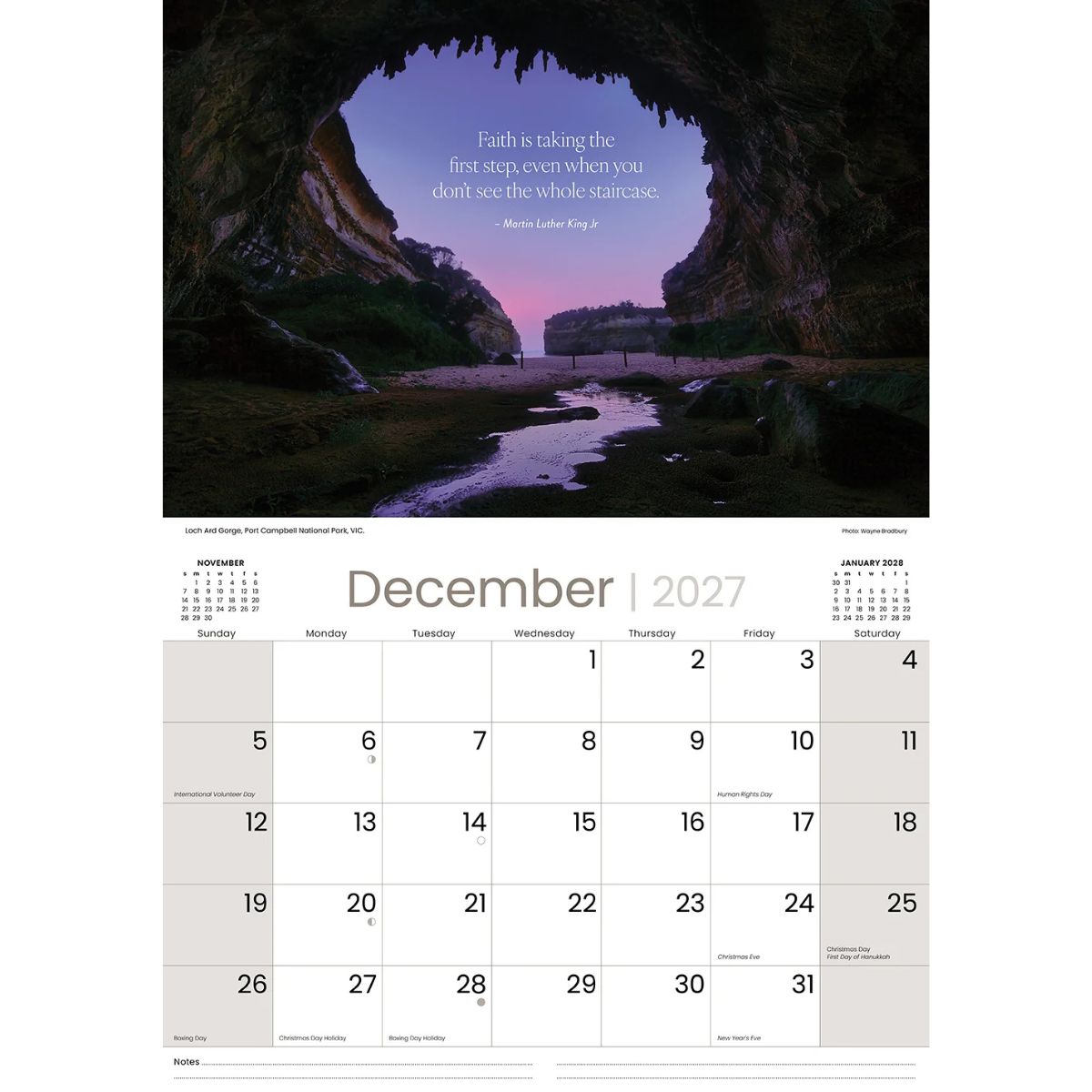 A single-page December 2027 calendar spread with a large scenic photograph of a cave opening over a stream at dusk, plus a minimalist monthly calendar grid below with a quote printed in the header area.