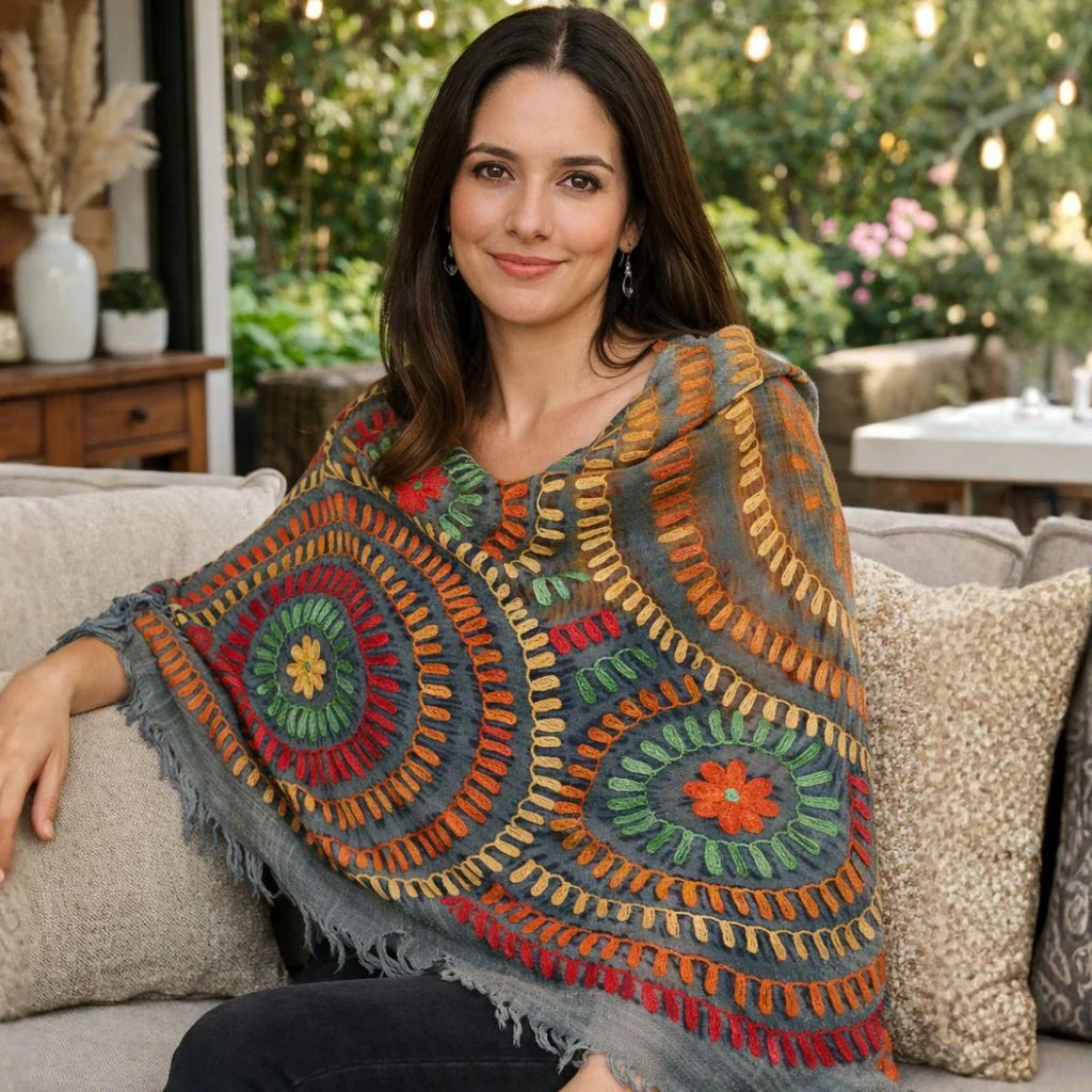 Woman wearing a colorful crocheted poncho sitting on a couch outdoors.