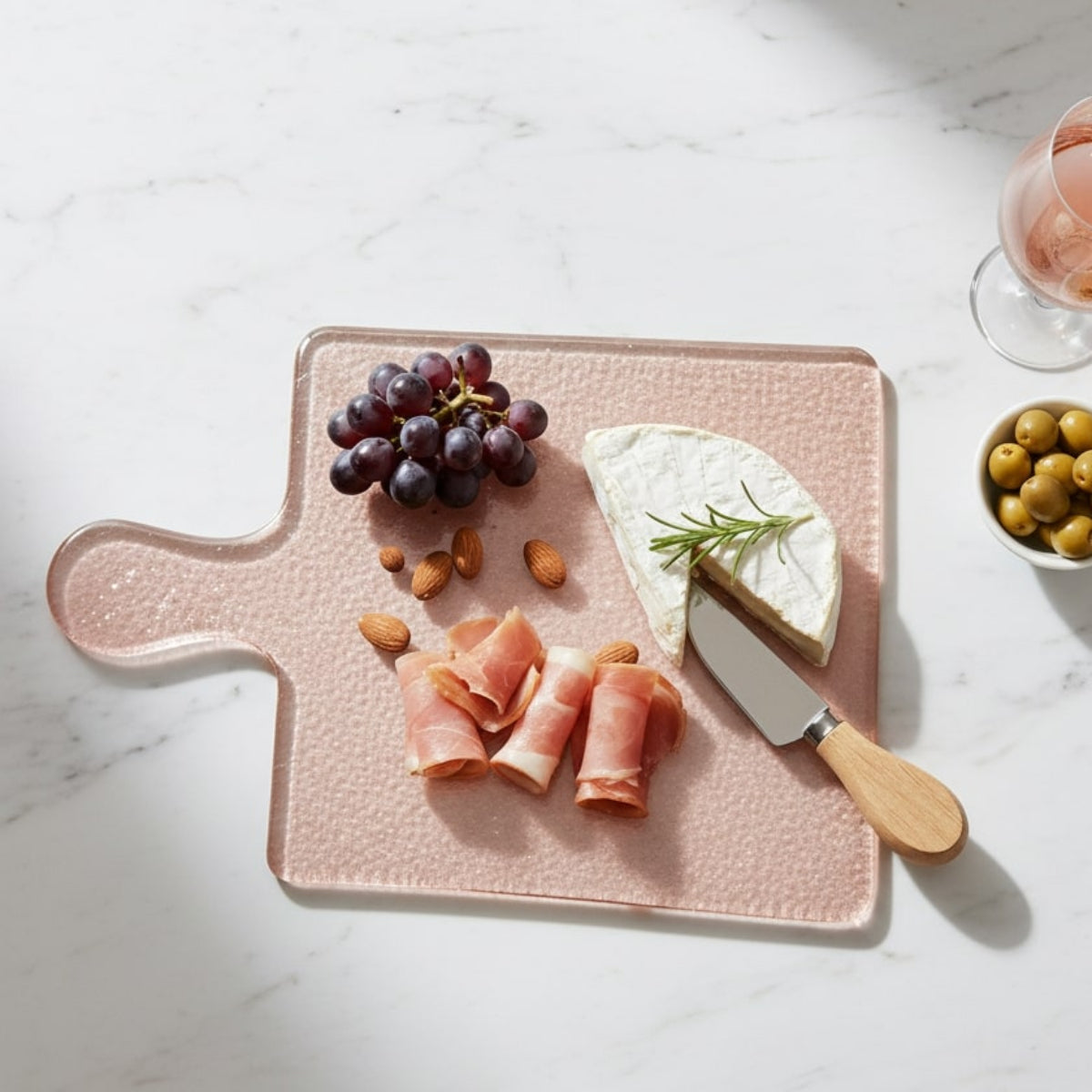 Pink cutting board with cheese, meat, and grapes on a marble surface