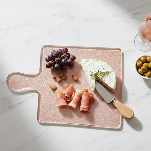 Pink cutting board with cheese, meat, and grapes on a marble surface