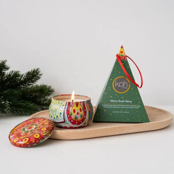 Colorful candle with decorative lid on a wooden tray next to a green tree-shaped packaging.