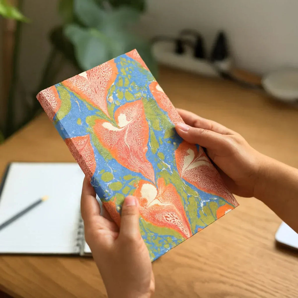 Person holding a notebook with a colorful floral cover on a wooden desk.