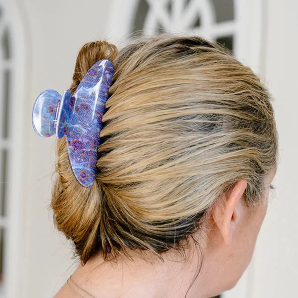 Person with a bun holding a decorative hair clip against a neutral background