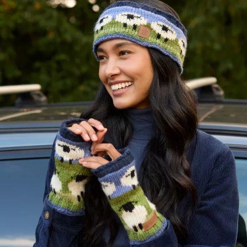Woman wearing a knitted headband and gloves with sheep design, standing outdoors.