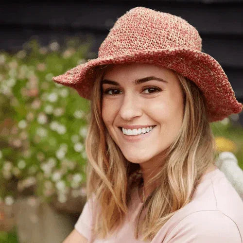 Woman wearing a pink straw hat with a blurred floral background