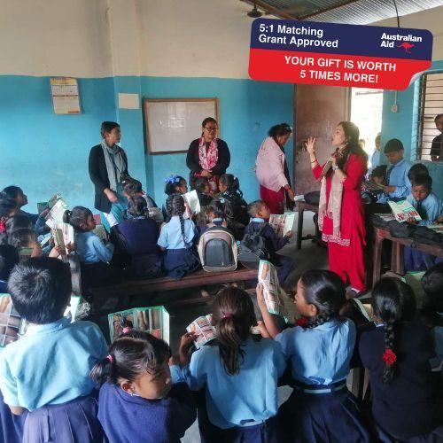 Children in a classroom with a teacher and an Australian Aid sign above.