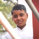 Young boy in a white shirt standing outdoors with a red structure in the background