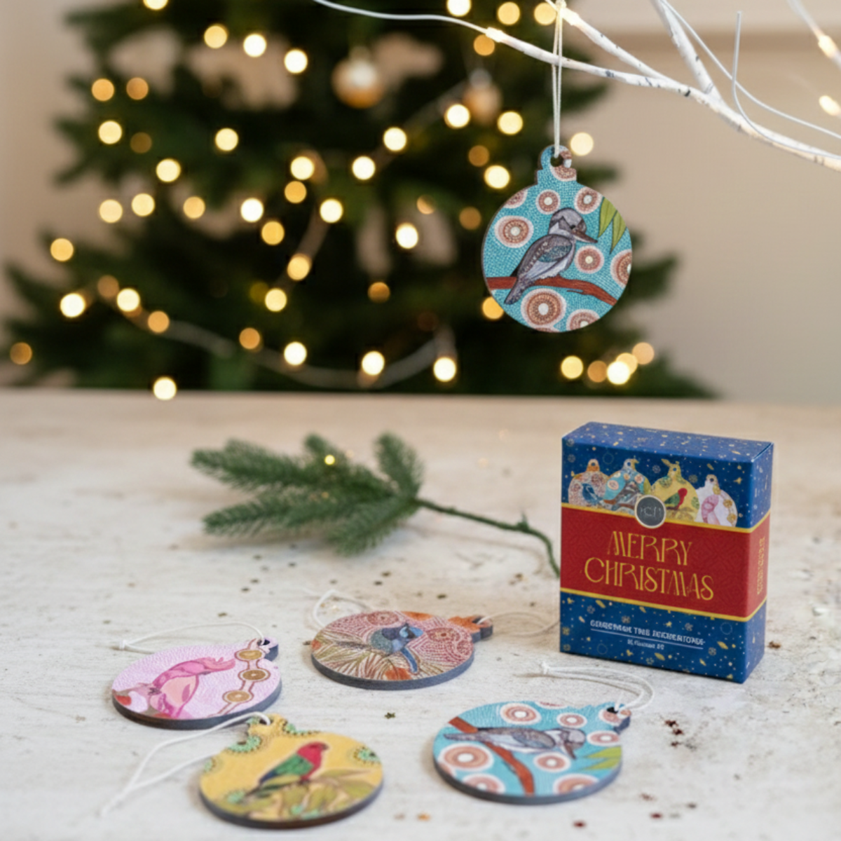 Colorful Christmas tree ornaments on a wooden surface with a decorated tree in the background.