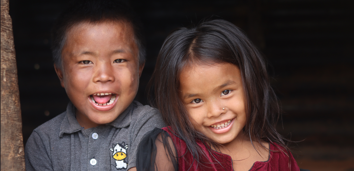 Two children smiling in front of a dark background