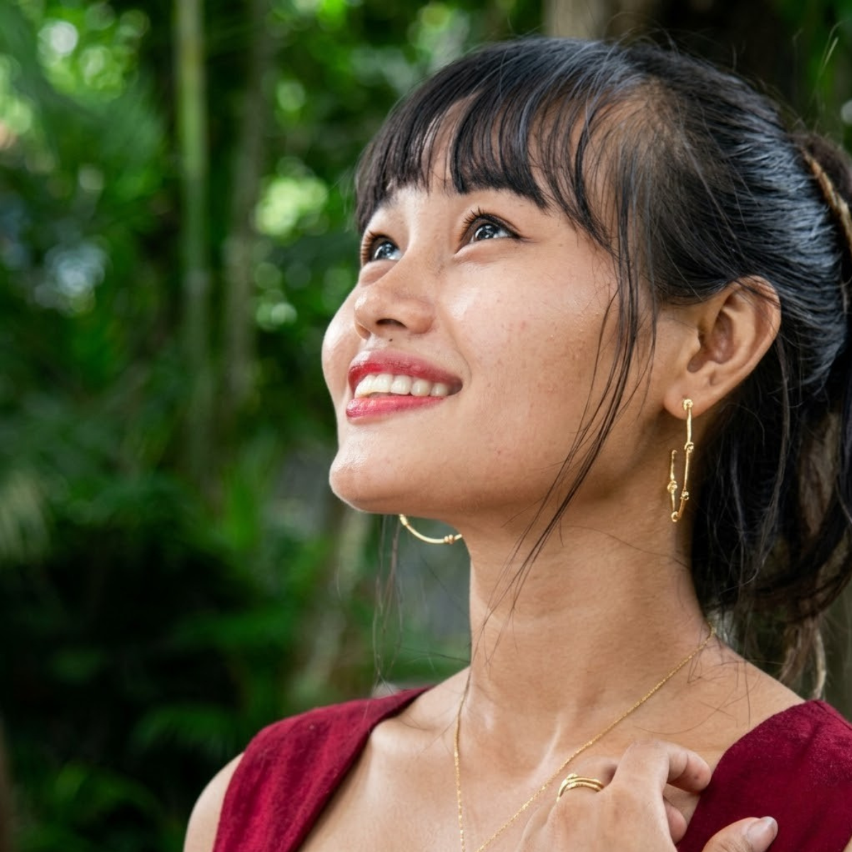 Woman with a side bun and gold earrings against a green blurred background