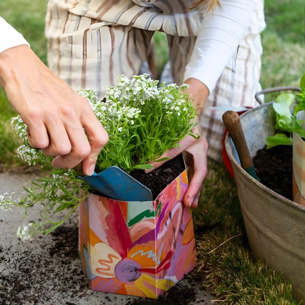 Person planting a small plant in a colorful pot with gardening tools nearby.