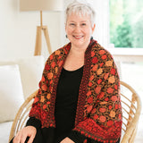 Woman sitting on a couch wearing a colorful patterned shawl in a bright room.